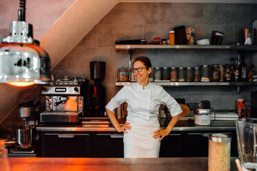 Weibliche Köchin in Uniform lächelnd in der Restaurantküche stehend - CAVF89481