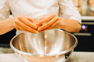 Weibliche Hände schlagen Eier in einer Metallschüssel in einer Restaurantküche auf - CAVF89485