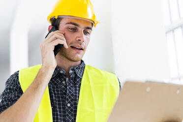 Architekt, der einen Notizblock hält, während er auf der Baustelle mit einem Mobiltelefon spricht - GIOF08850