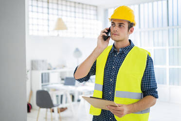 Young man talking on mobile phone while standing at office under construction - GIOF08853
