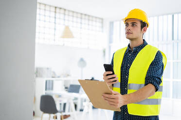 Architekt hält Notizblock und telefoniert auf der Baustelle - GIOF08854