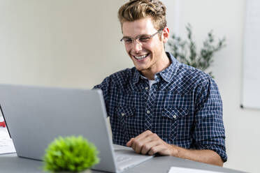 Lächelnder Mann, der einen Laptop benutzt, während er im Büro sitzt - GIOF08862