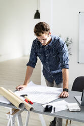Architect analyzing blueprint while standing by desk at office - GIOF08865