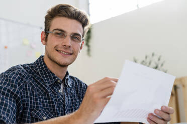 Smiling man holding paper while working at office - GIOF08892