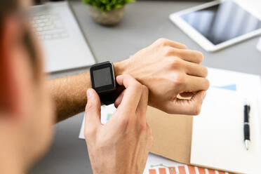 Man looking at smart watch while sitting by desk at office - GIOF08898