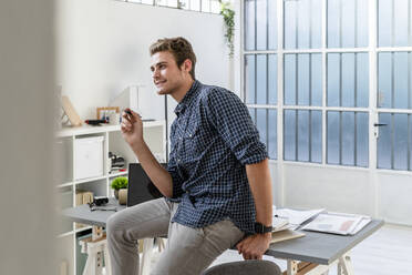 Lächelnder Architekt, der einen Stift hält, während er an einem Tisch sitzt - GIOF08912