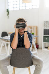 Architect smiling while using visual reality simulator sitting on chair at office - GIOF08914