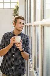 Man looking through window while standing at office - GIOF08920