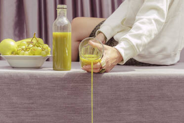 Close-up of woman throwing green juice while sitting on table at home - ERRF04446
