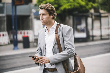 Mann mit Tasche, der ein Mobiltelefon benutzt, während er in der Stadt steht - UUF21565