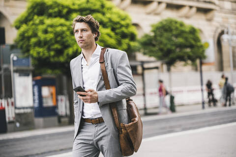 Man with bag using mobile phone while walking in city stock photo