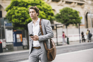 Mann mit Tasche benutzt Mobiltelefon beim Spaziergang in der Stadt - UUF21566