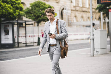 Geschäftsmann benutzt Mobiltelefon beim Spaziergang in der Stadt - UUF21568