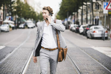 Mann mit Tasche, der in einer Straßenbahn in der Stadt mit seinem Handy telefoniert - UUF21572