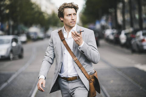 Man with bag talking on phone while walking at tramway in city stock photo