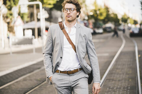 Handsome man with hands in pockets walking on tramway in city stock photo
