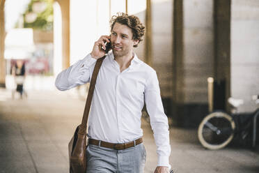 Mann lächelt, während er in der Stadt mit einem Mobiltelefon spricht - UUF21582