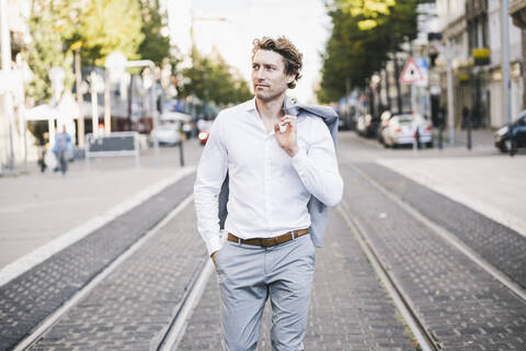 Man standing with hand in pocket and jacket over shoulder in city stock photo