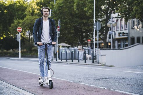 Mann hört Musik, während er in der Stadt mit einem elektrischen Roller fährt - UUF21591