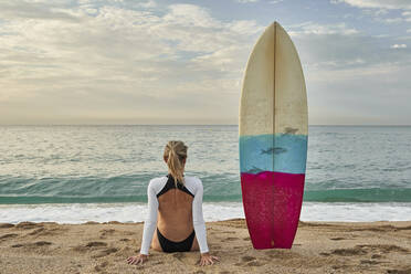 Woman sitting by surfboard on sand at beach - VEGF02926