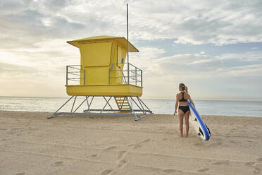 Frau hält Surfbrett am Strand während des Sonnenuntergangs - VEGF02928