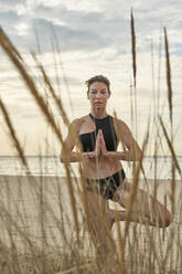 Frau übt Yoga im Stehen am Strand - VEGF02930