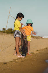 Friends collecting garbage while standing on beach - ERRF04457