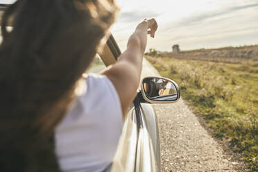 Young woman pointing towards cloudy sky while sitting in car - ZEDF03789