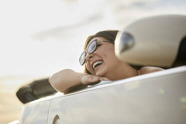 Fröhliche Frau lacht, während sie in einem Cabrio für eine Autoreise sitzt - ZEDF03795