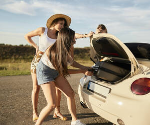 Female friends removing suitcase from car trunk - ZEDF03800