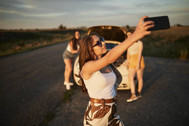 Young friends taking selfie while standing on road during sunset - ZEDF03818