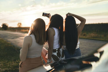 Weibliche Freunde, die ein Selfie machen, während sie bei Sonnenuntergang auf der Straße stehen - ZEDF03819