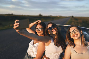 Lächelnde Freunde, die ein Selfie machen, während sie bei Sonnenuntergang auf der Straße stehen - ZEDF03820
