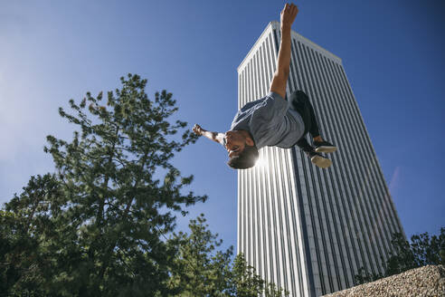 Young man jumping while performing parkour against Torre Picasso in city - ABZF03327
