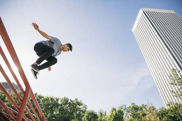 Young man performing parkour over railing against clear sky in city - ABZF03329