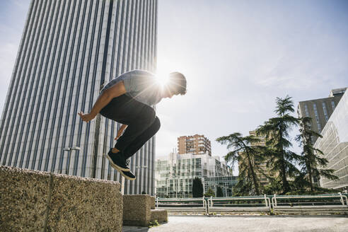 Young man performing parkour over retaining wall against Torre Picasso in city - ABZF03330