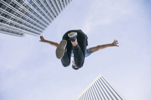 Junger Mann beim Parkour gegen den Himmel in der Stadt - ABZF03331