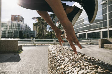 Legs of young man jumping over wall performing parkour in city - ABZF03332