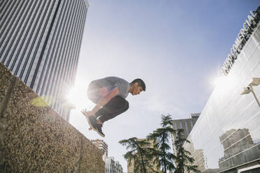 Young man performing parkour over retaining wall against Torre Picasso - ABZF03338