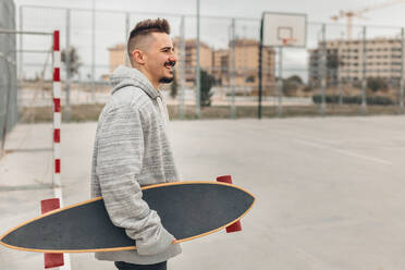Porträt eines jungen Mannes im Freien mit einem Skateboard in der Hand - MRRF00478