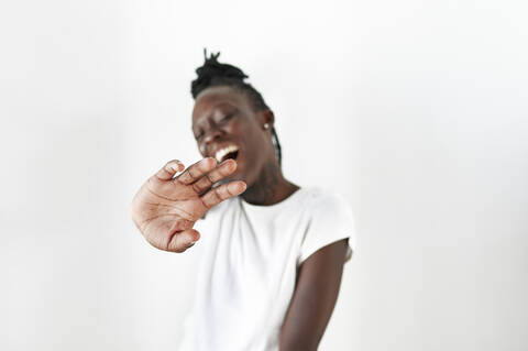 Cheerful young woman showing hand while standing against white background stock photo