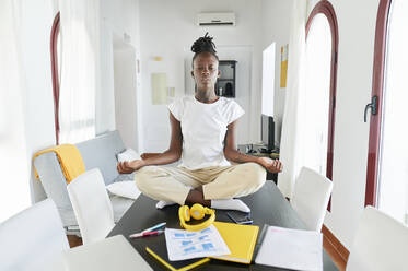 Geschäftsfrau beim Meditieren mit Laptop und Buch auf dem Schreibtisch zu Hause - KIJF03282