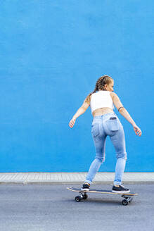 Frau fährt Skateboard auf der Straße vor einer blauen Wand - PGF00035