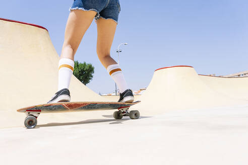 Beine einer jungen Frau beim Skateboardfahren auf einer Sportrampe vor blauem Himmel im Park - PGF00055
