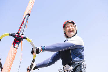 Fröhlicher älterer Mann beim Windsurfen gegen den klaren Himmel an einem sonnigen Tag - PGF00060