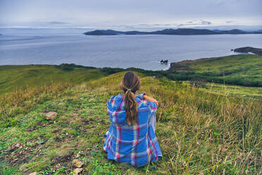 Frau schaut auf das Japanische Meer, während sie auf einem Berg sitzt, Halbinsel Krabbe, Primorje, Russland - KNTF05430