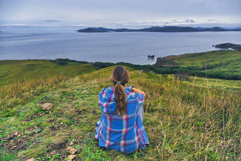 Frau schaut auf das Japanische Meer, während sie auf einem Berg sitzt, Halbinsel Krabbe, Primorje, Russland - KNTF05430