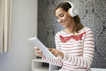 Smiling woman listening music over headphones while using digital tablet at home - JSMF01713