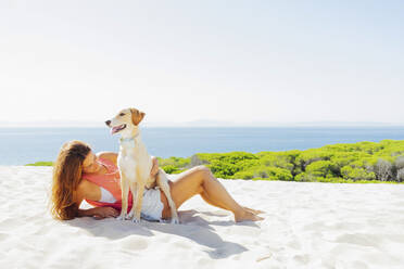 Frau mit Hund entspannt am Strand gegen den klaren Himmel an einem sonnigen Tag - PGF00072