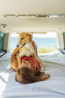 Frau mit Hund auf dem Bett im Wohnmobil liegend - PGF00075